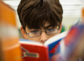 boy reading a book looking through the stacks